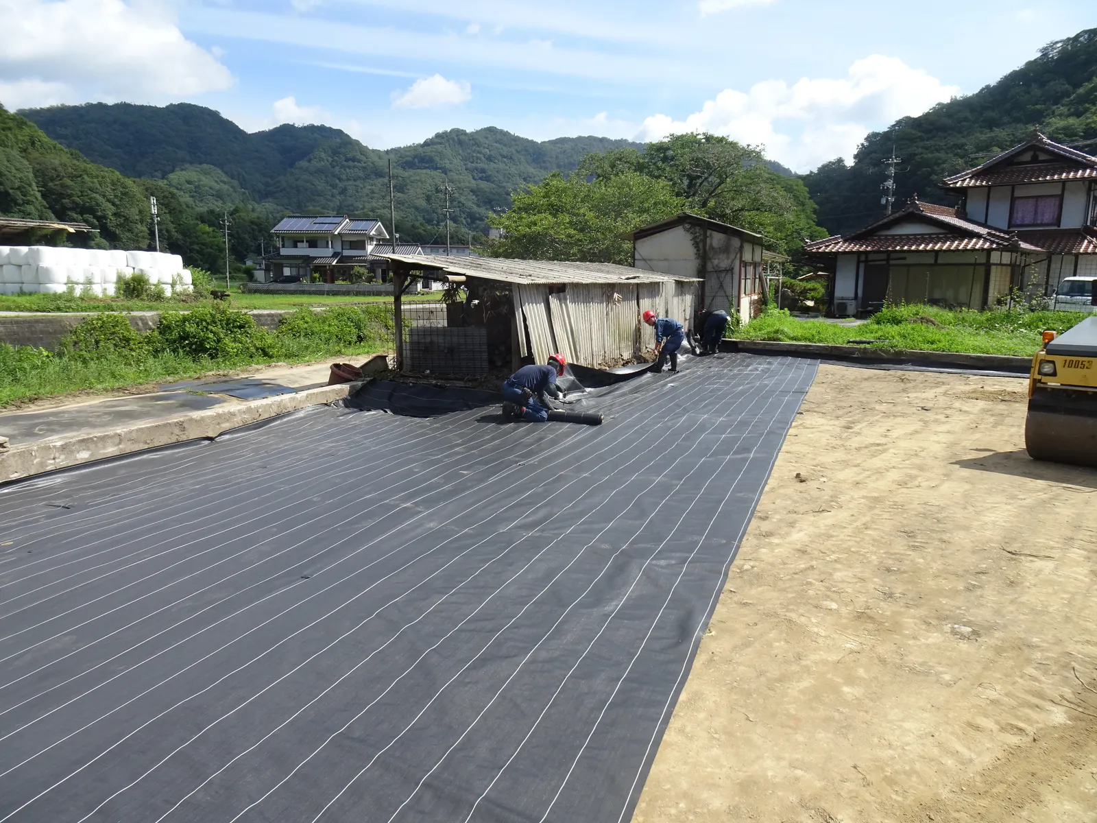 竹原市民間雑種地改善工事で防草シートを敷設する作業風景